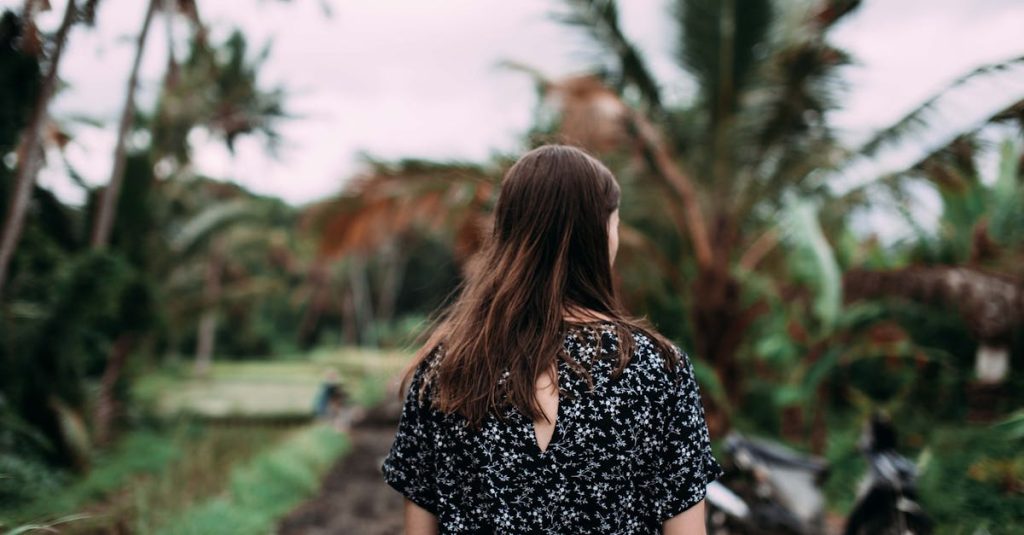 Back view of a woman walking along a tropical path with palm trees, showcasing a serene outdoor setting.